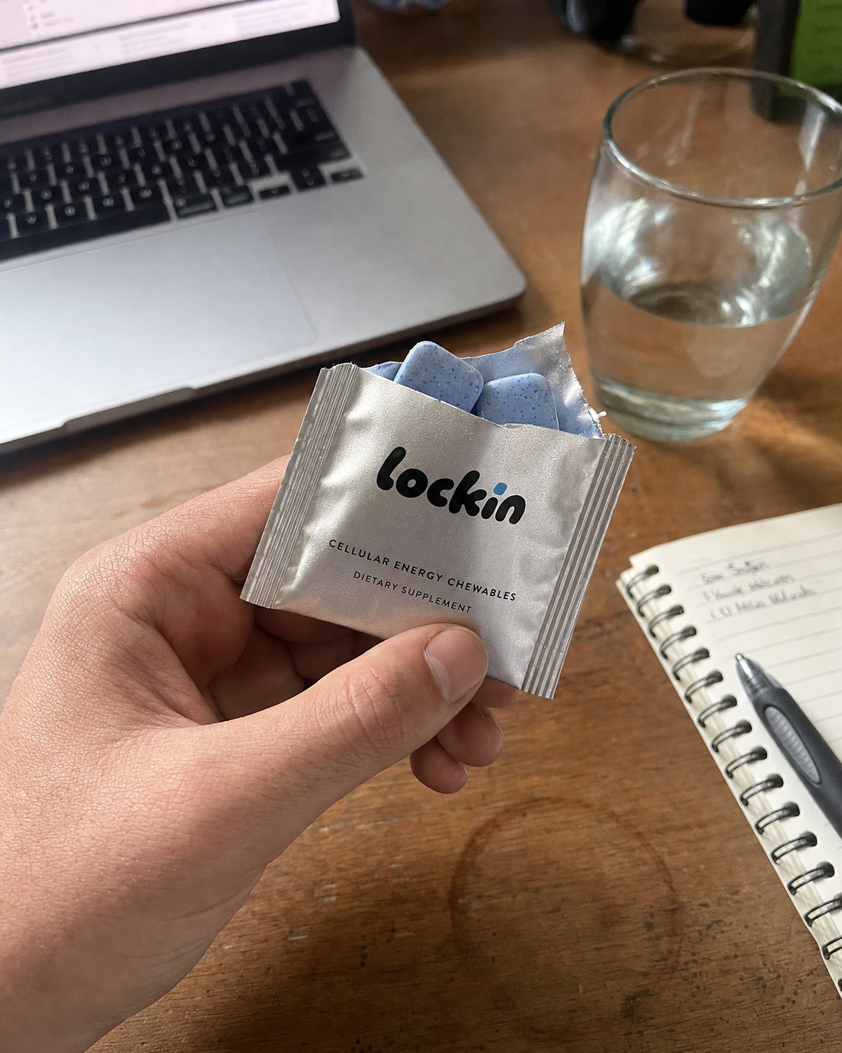 A hand holding a torn foil over a desk with a laptop and a glass of water